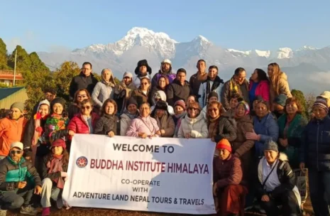 An international tour group of 42 travelers from Mexico, Peru, USA, and France posing at Australian Camp, Nepal, with the massive snow-capped peaks of Mount Fishtail (Machapuchare) and the Annapurna mountain range visible in the background.