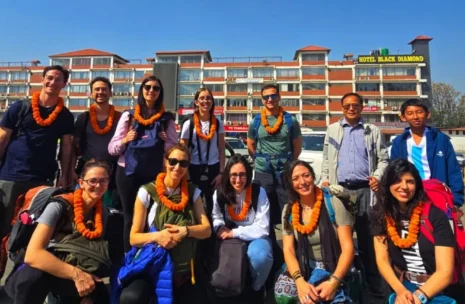 Best Nepal Tour - A diverse group of Italian travelers smiling and posing with an expert local guide in front of the ancient, golden-topped Boudhanath Stupa in Kathmandu, Nepal, under a bright blue sky with prayer flags fluttering in the background.